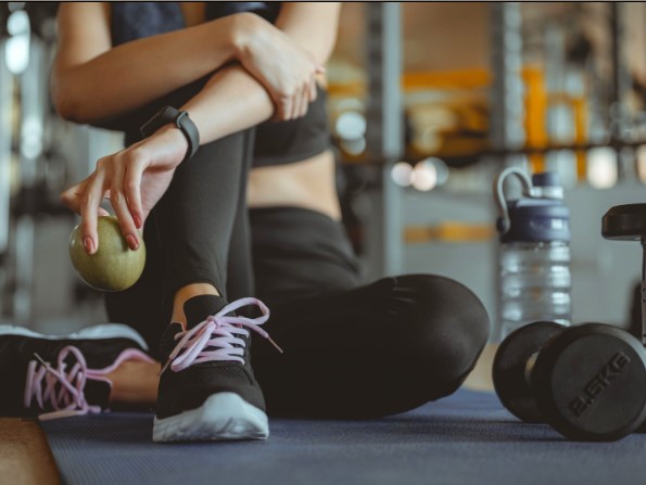 Woman sitting on gym mat with dumbbell and water bottle nearby